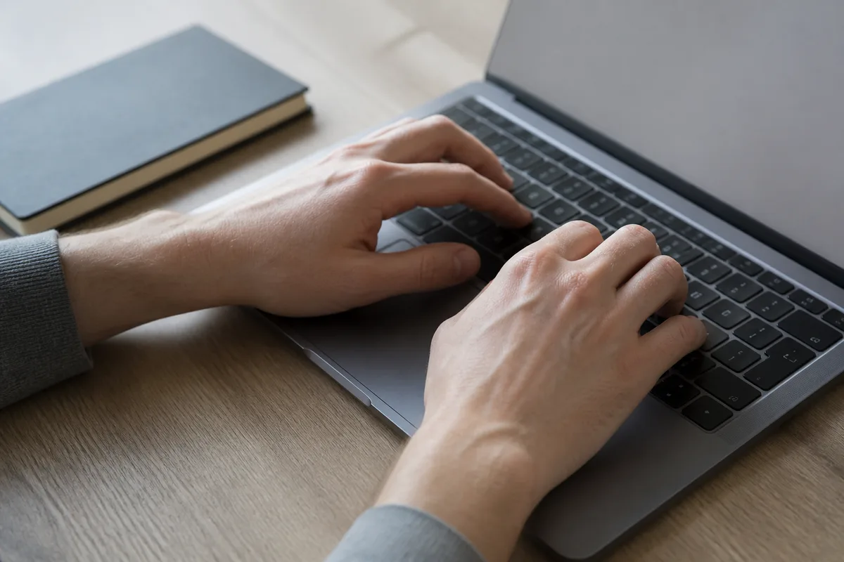 Mains posées sur le clavier d’un ordinateur portable dans un bureau clair
